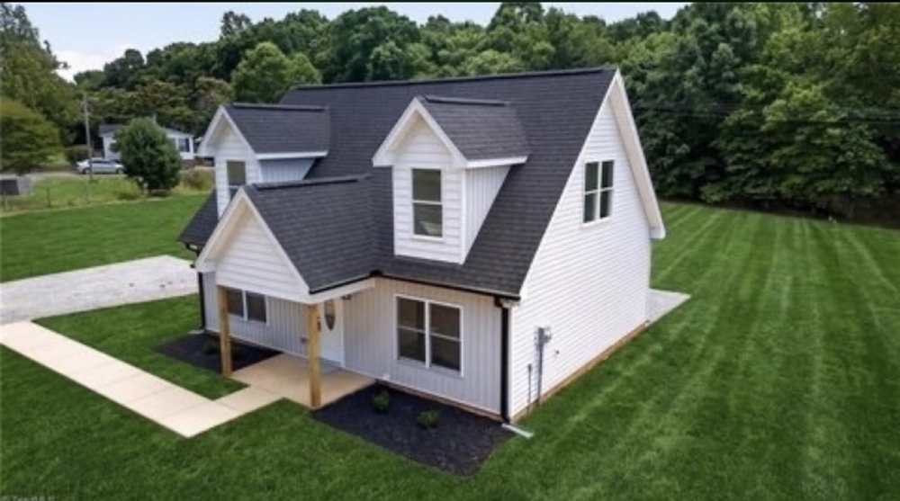 White farmhouse with a charcoal roof, gabled dormers, and a covered entry on a green lawn